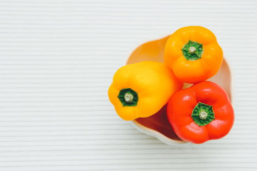 白い木目テーブルに置いた黄色とオレンジと赤のパプリカ3個