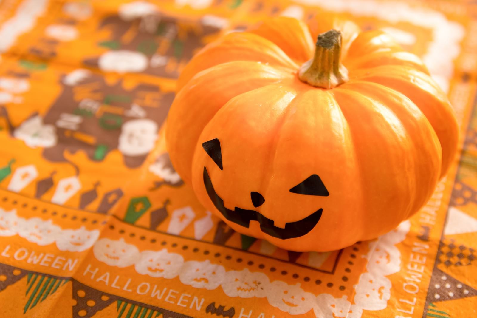 ハロウィン柄の紙の上に置かれた、顔が彫られたオレンジ色のかぼちゃ