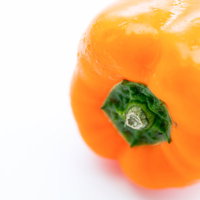 白い背景に置かれた黄色いパプリカ、緑のヘタ付きの写真