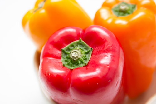 黄と赤のパプリカが白い背景に並ぶ新鮮な野菜