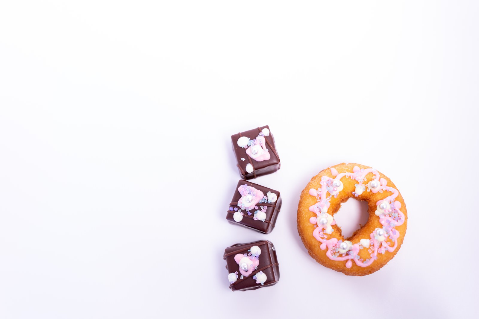 ピンク色でデコレーションされたドーナッツとチョコレートケーキが白い背景に並んでいる