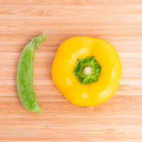 木目調まな板に並ぶえんどう豆とパプリカの新鮮な野菜の写真