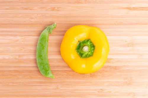 木目調まな板に並ぶえんどう豆とパプリカの新鮮な野菜