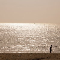 夕焼けに染まる海岸で立つ人影の写真