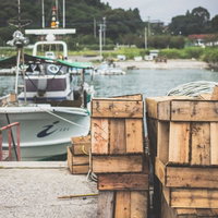 漁港に積み上げられた木製の漁具と漁船の風景の写真