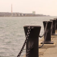 チェーンで繋がれた黒い係船柱が並ぶ港の写真