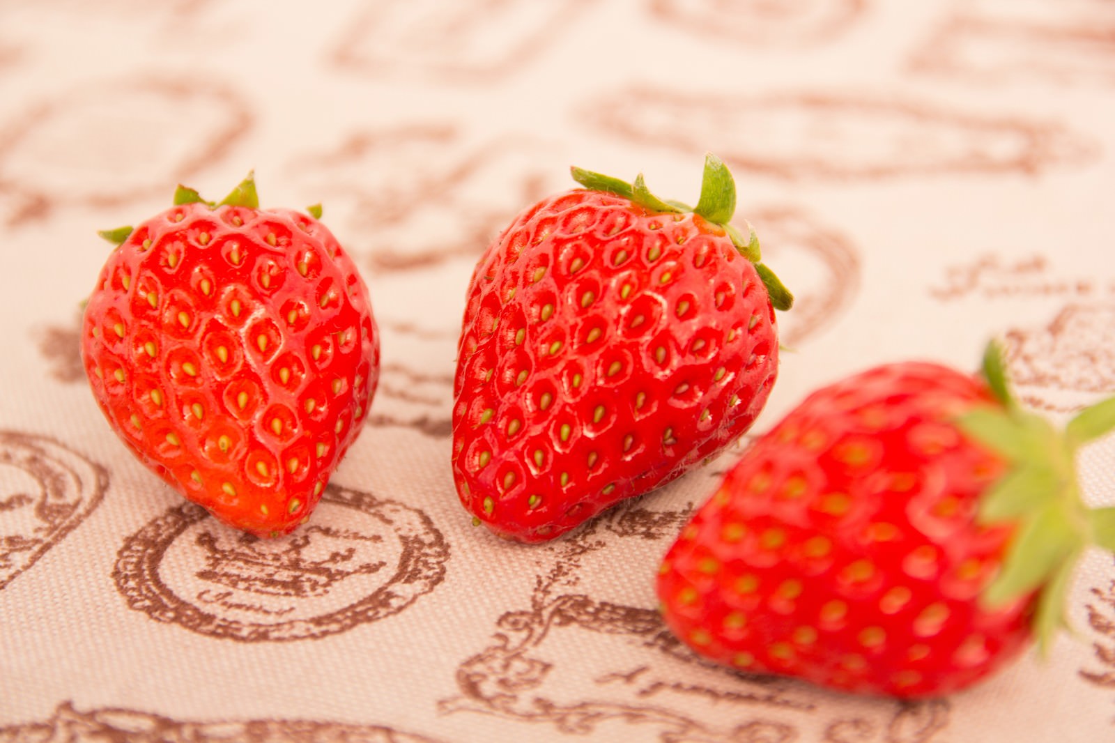 古い布地の上に並んだ3つの新鮮なイチゴ。緑の葉がついている