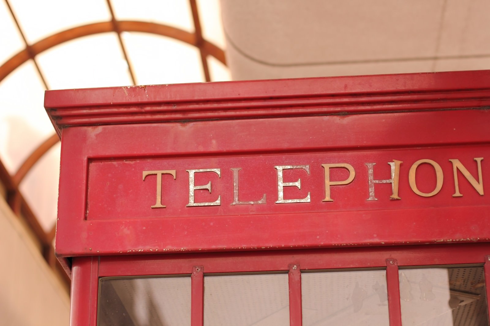 赤い電話ボックスの上部に金色のTELEPHONEの文字が彫られた看板が見える