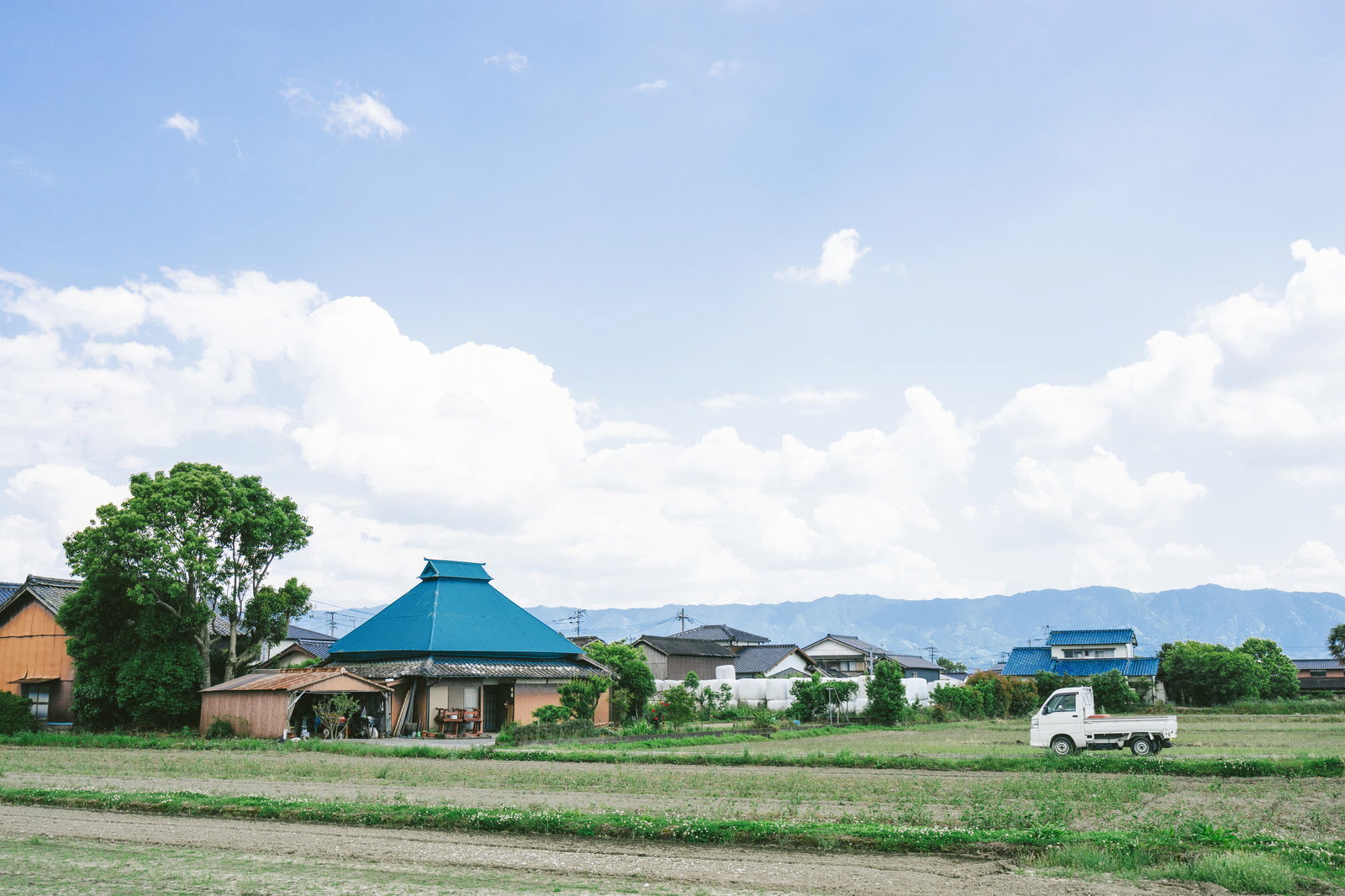 畑と青い屋根の建物が広がる農村風景