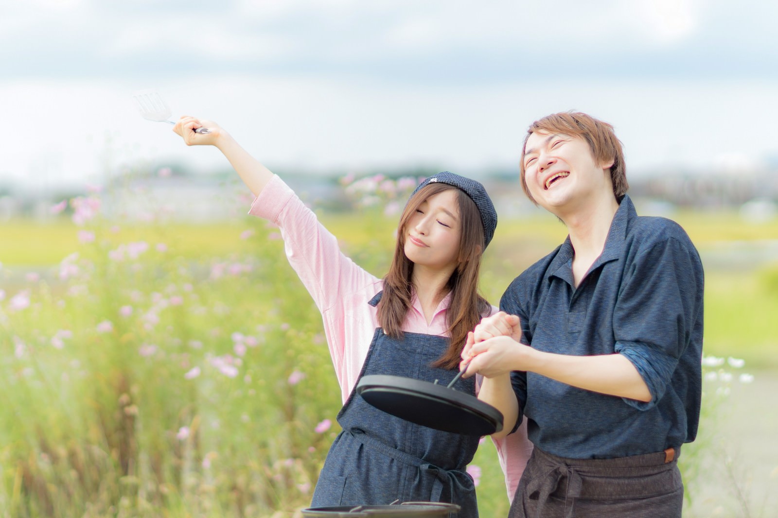 田園でダッチオーブンを囲む笑顔の女性二人［モデル：五十嵐夫妻］