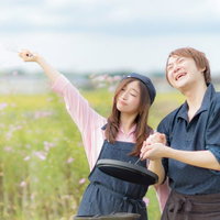 田園風景の中でダッチオーブンを楽しむ夫婦の写真