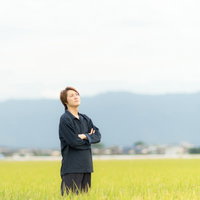 広大な田んぼで腕を組んで考える農家の男性の写真