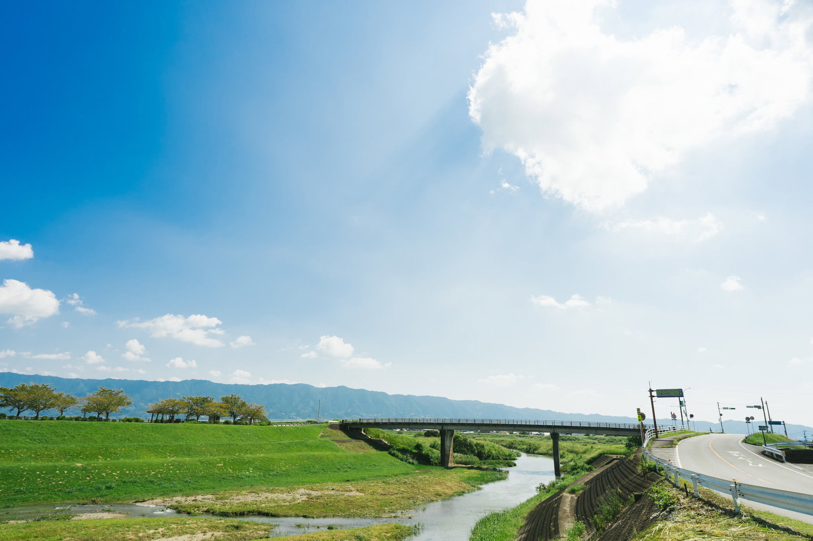青空の下、大刀洗の小石原川沿いに広がる緑の河川敷と橋