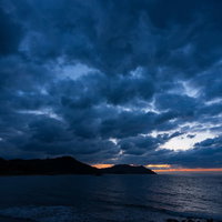 島の上に沈む夕日と暗い雲がたなびく日没の海景の写真