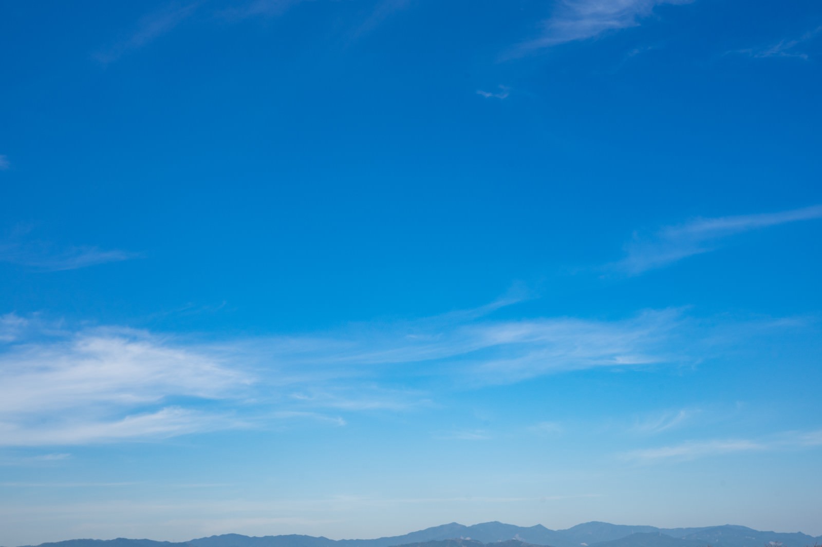 青空と白い雲、遠くに山並みが見える晴天