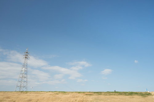 河川敷に立つ高圧送電鉄塔と青空の風景