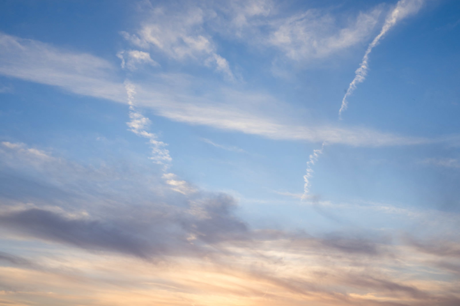 夕暮れと青空のグラデーションに飛行機雲が伸びる空