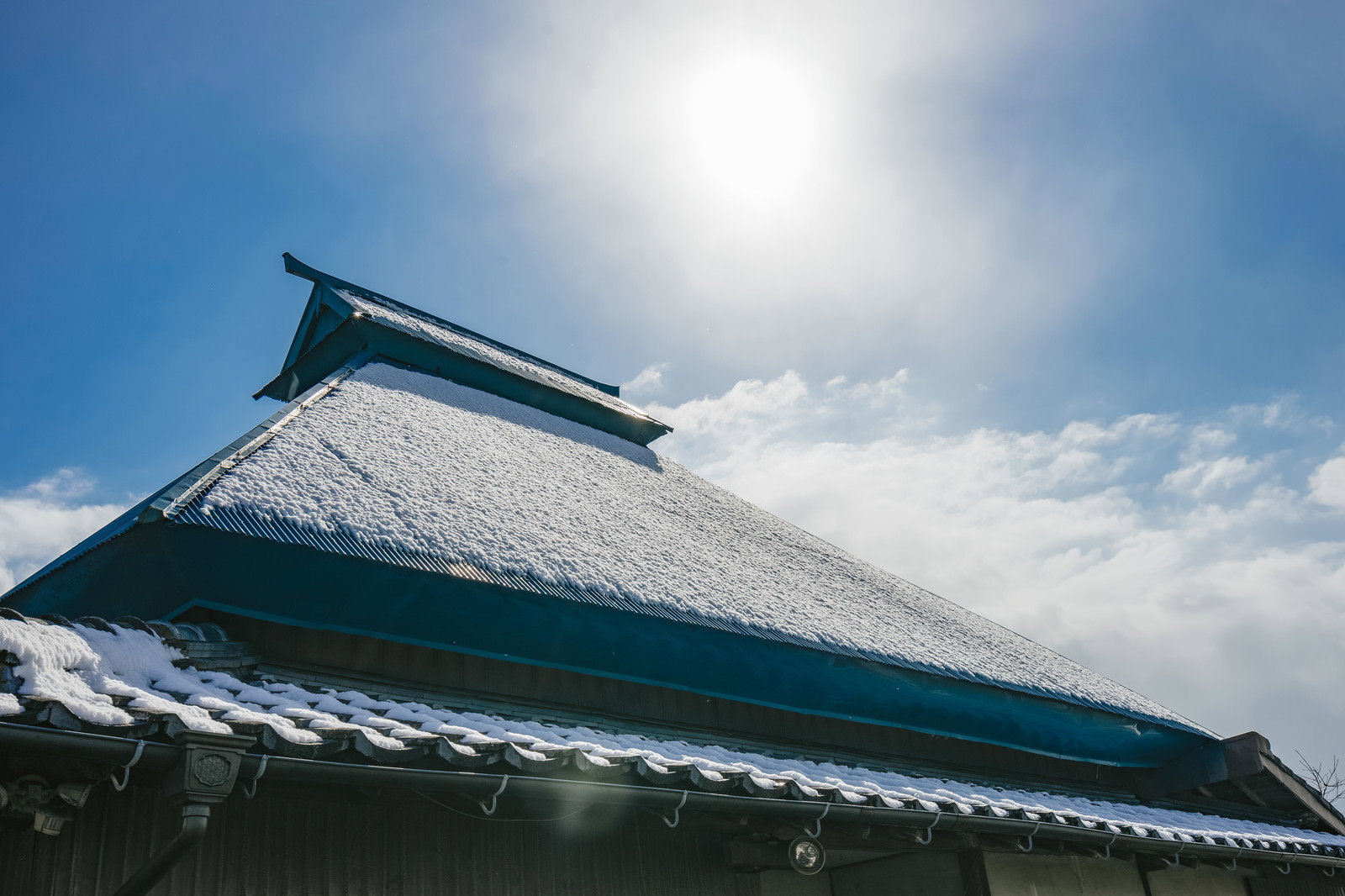 薄く雪が残る青緑の瓦屋根と快晴の青空