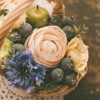 ピンクや青紫の花と緑の実が入った籐のバスケットアレンジの写真