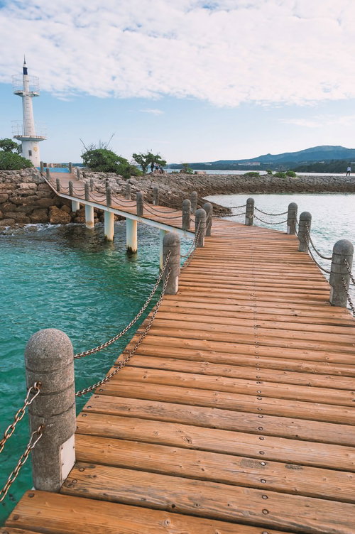 石の柱とチェーンの手すりがある木の桟橋と白い灯台