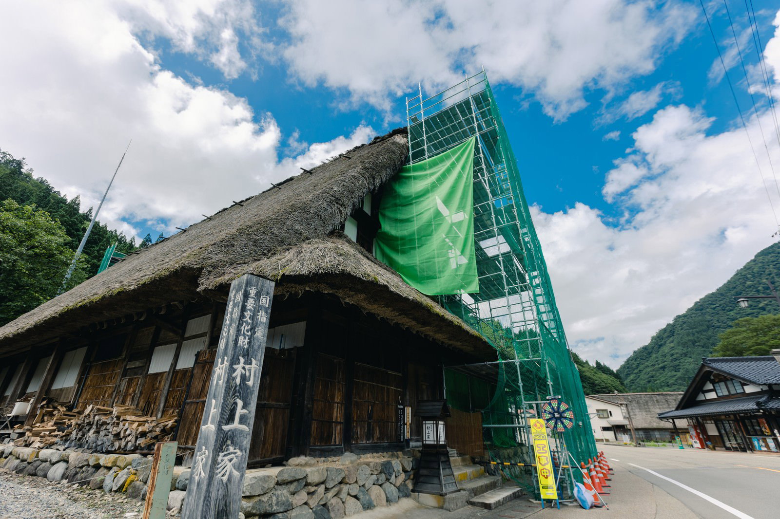 緑の養生シートで覆われた合掌造りの村上家と工事用足場