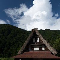 立ち上がる雲と南砺市菅沼集落のお食事処の合掌造り建物の写真