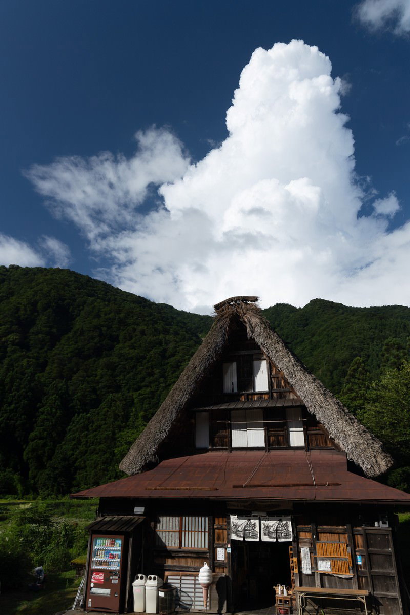 青空と雲を背景に山間に佇む菅沼集落の合掌造りお食事処