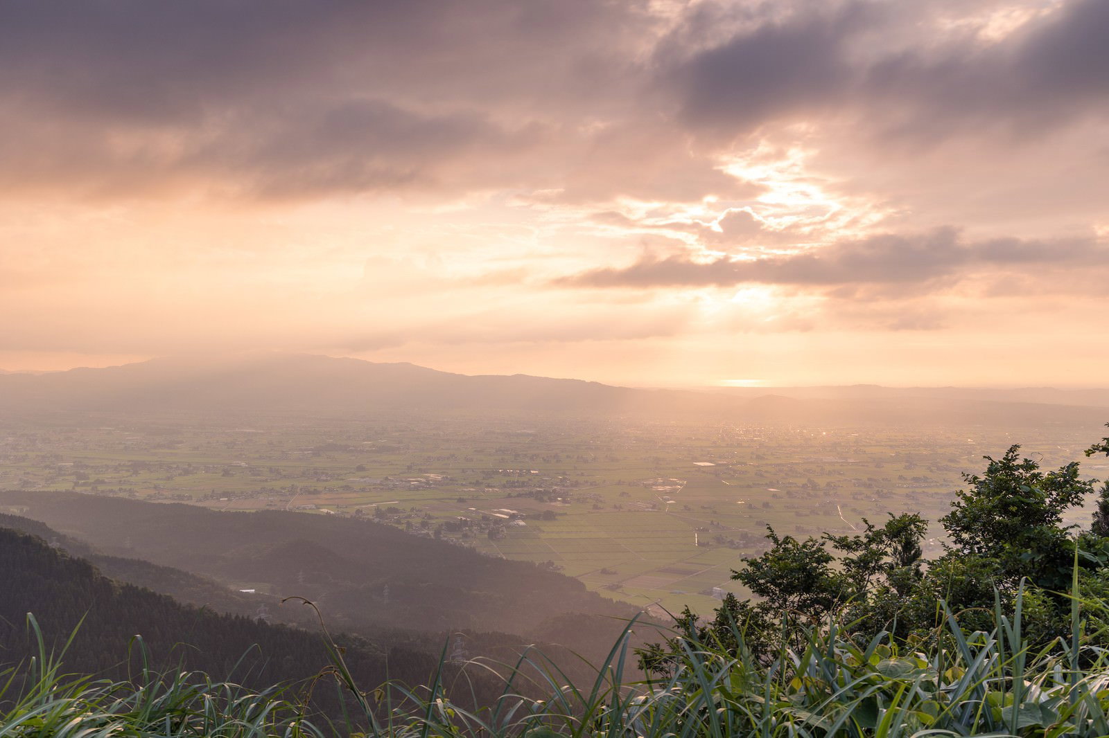 雲間から差し込む天使の梯子が夕焼けに染まった散居村を照らす風景