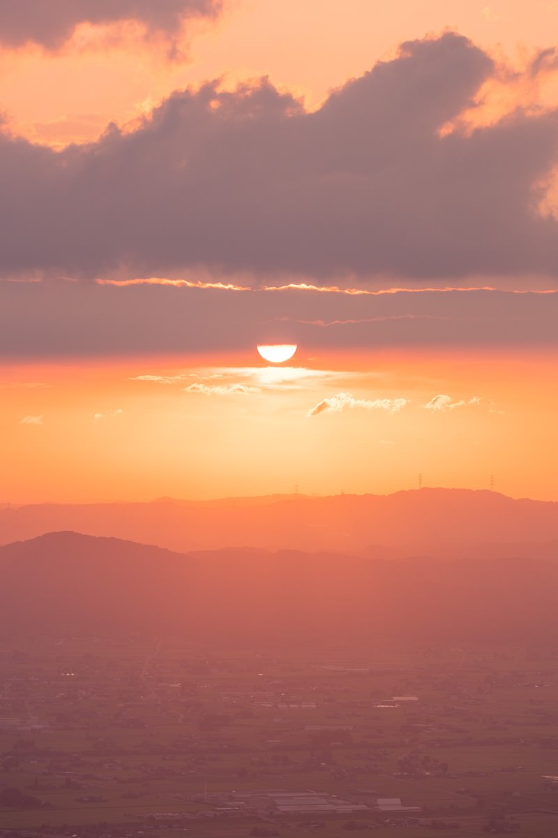 夕日が沈む中、オレンジ色の空の下に散居村の家屋が点在する田園風景