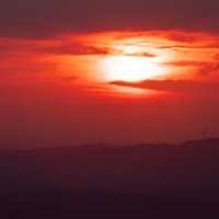 真っ赤に燃える太陽と山々のシルエット、夕焼けの風景の写真