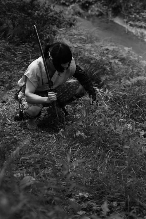 刀を肩にかけて川沿いの竹林に座り込む山賊