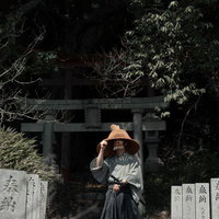 笠から零れ落ちる光、鳥居と奉納石柱前に立つ侍の武士の写真