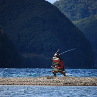 湖畔の中州で太刀を構える赤い大鎧の武士の写真