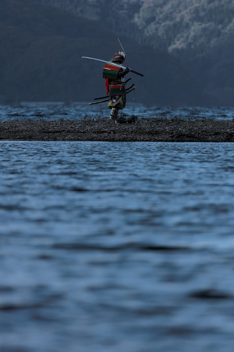 湖畔の中州で刀を肩に担ぐ大鎧姿の侍［モデル：まーこ］