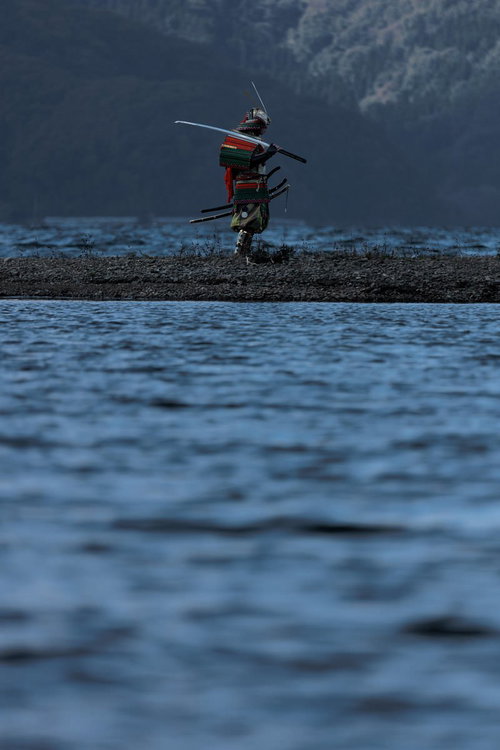 湖畔の中州に立ち、刀を肩に担いで大鎧で武装する侍