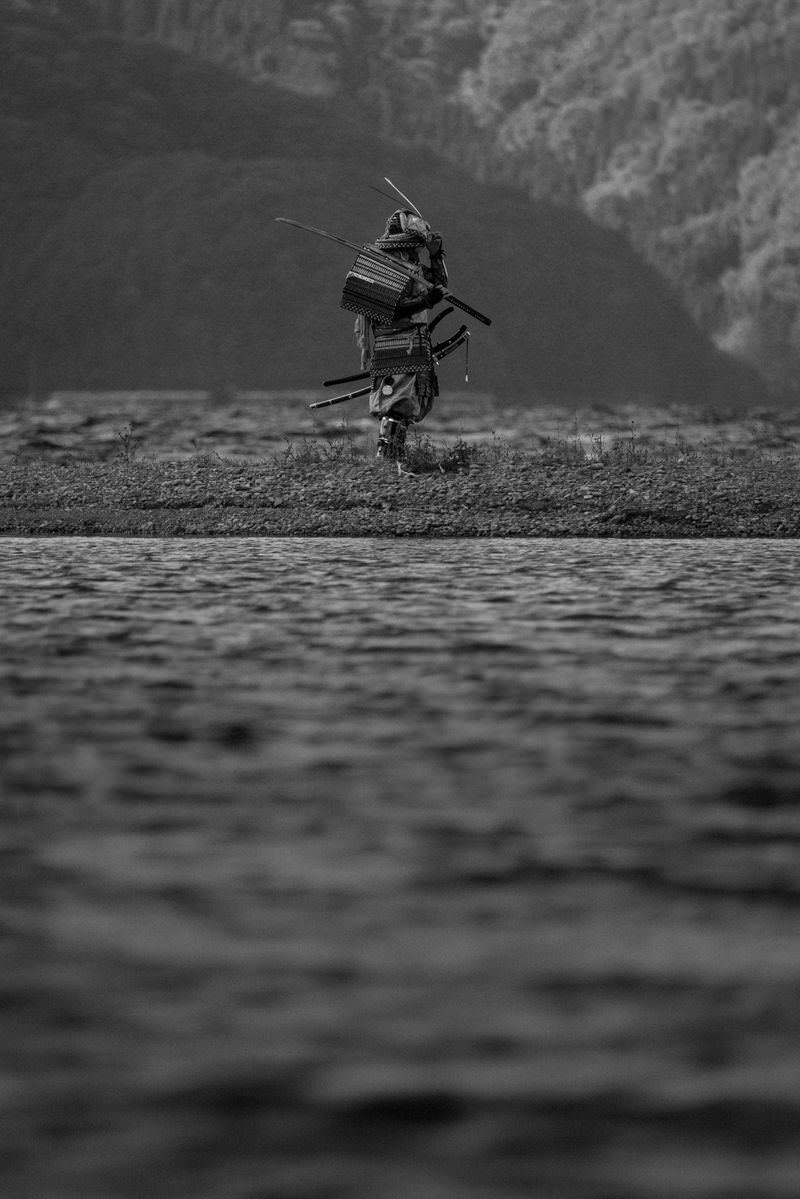 中州に立ち刀を肩に担ぐ甲冑姿の侍をモノクロで撮影した写真［モデル：まーこ］