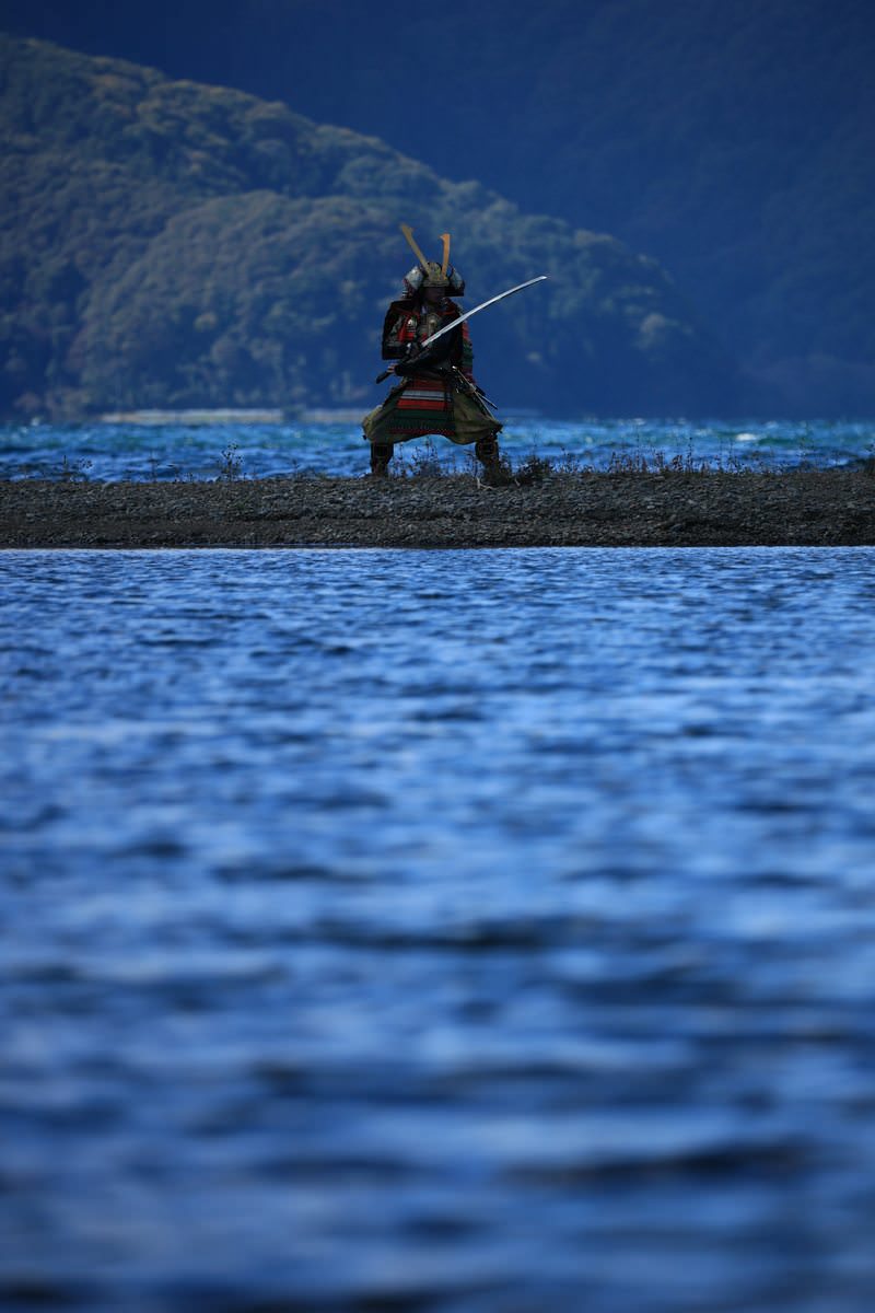 Samurai in full armor wielding a sword on the blue-watered sandbars
