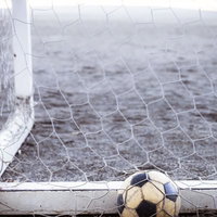 白いネットの下に置かれた使い込んだサッカーボールの写真