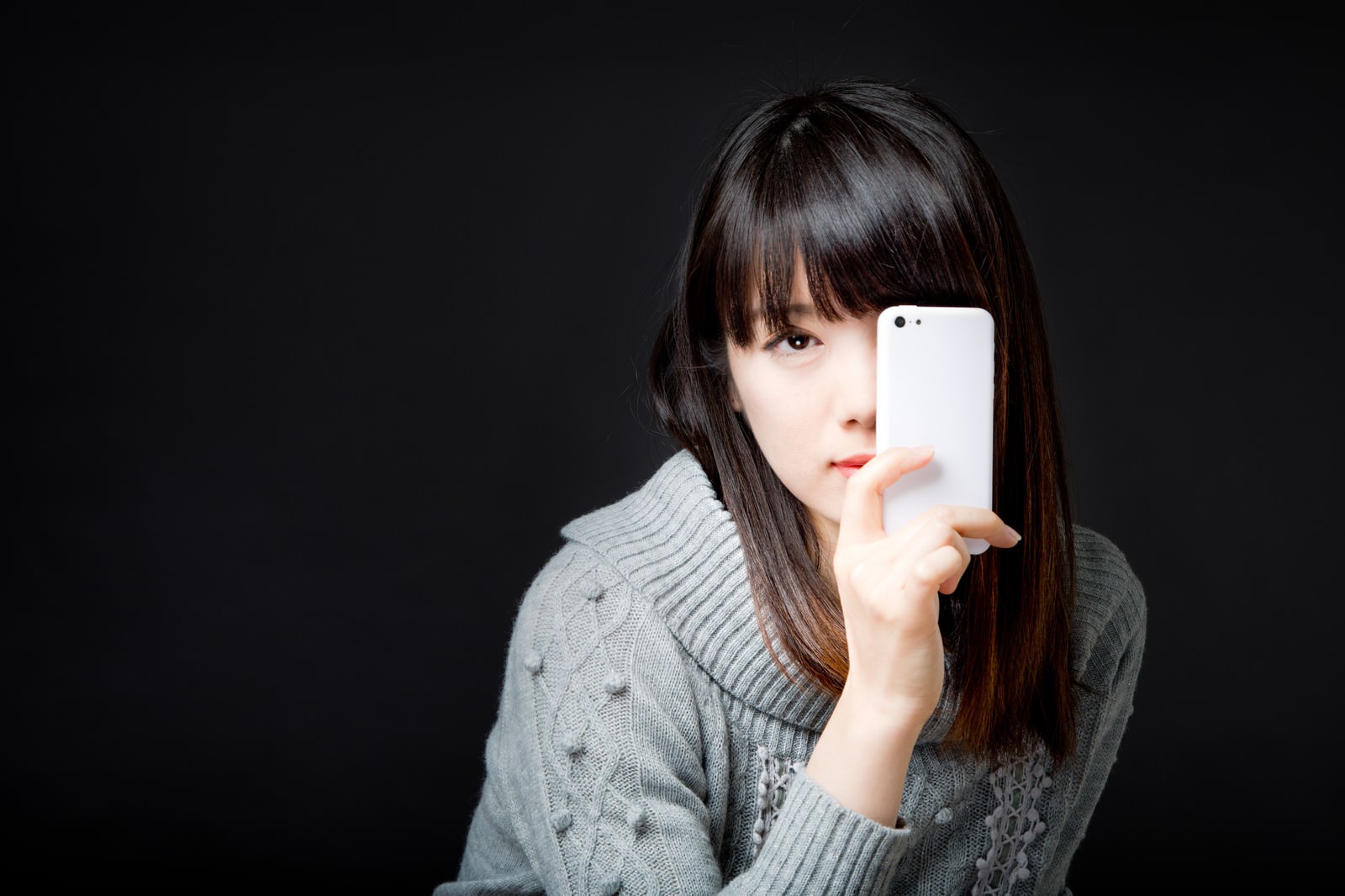 スマートフォンを持ち上げて注意を促す黒髪の女性［モデル：モデルリリース］
