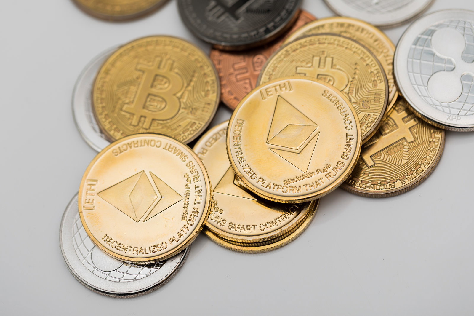 ETHイーサリアムのロゴが刻印された金色のコインと重なる各種通貨