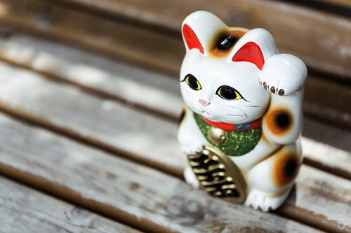 木製ベンチに座った白い招き猫の置物、金運アップと商売繁盛の縁起物