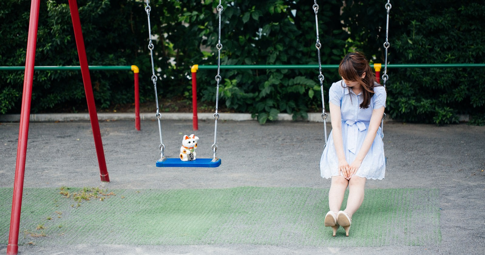 公園のブランコに座る女性と隣に置かれた招き猫［モデル：モデルリリース］