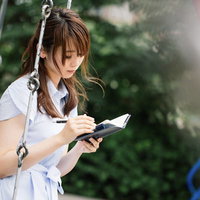 公園のブランコで手帳に向き合い悩む女性の心理描写の写真