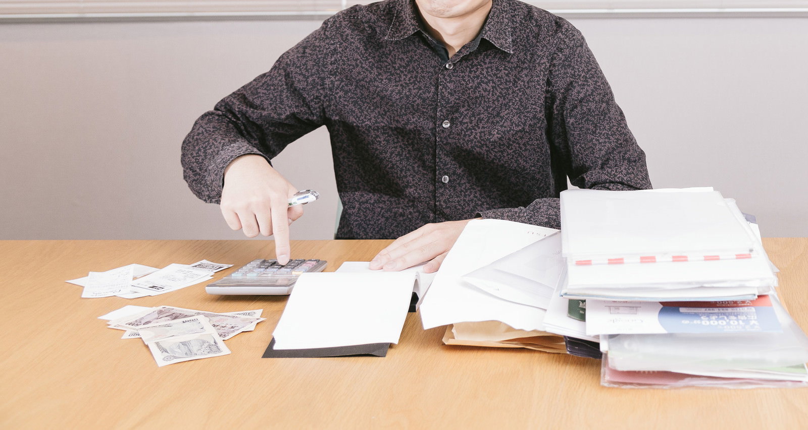 木製机で領収書と書類を確認しながら計算機を操作する男性