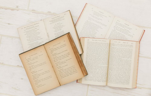 白いテーブルに開いた複数の洋書としおり、古い書籍の積み重ね