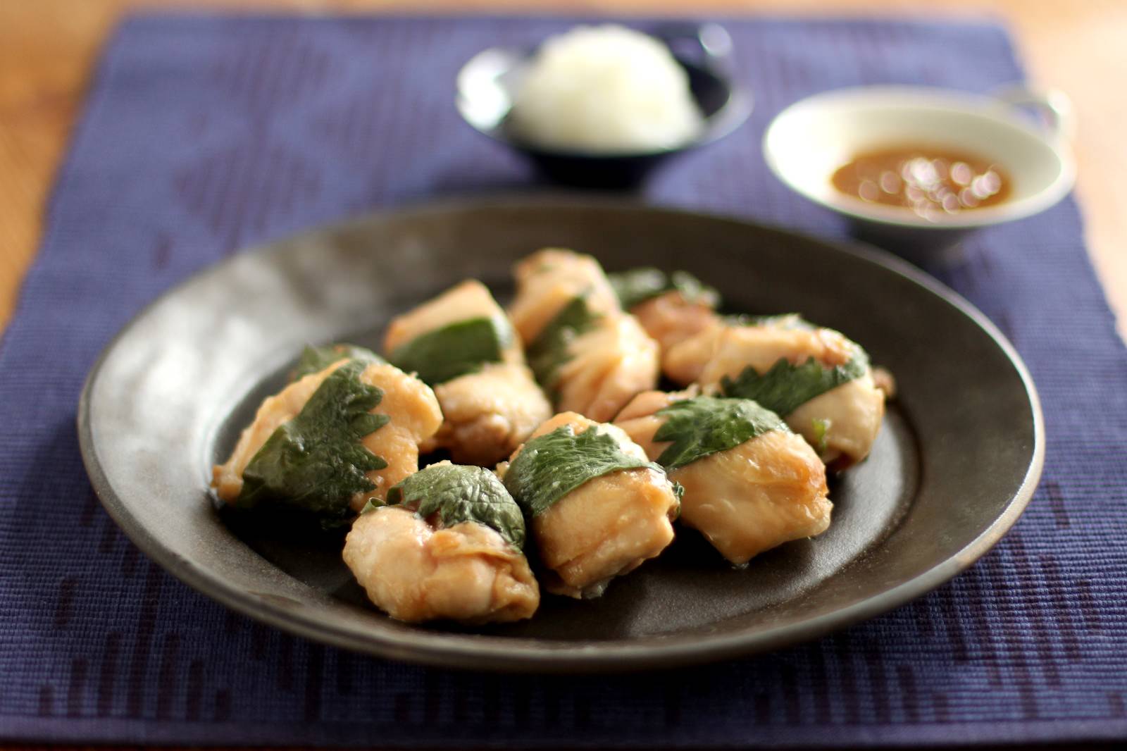 青のりで巻いた焼いた鶏肉の磯辺巻きが黒い皿に盛られ、たれと大根おろしが添えられている