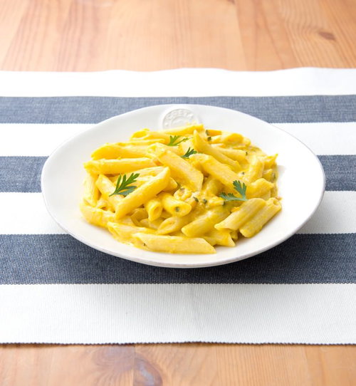 木のテーブルに盛られたハーブ飾りのかぼちゃクリームペンネ