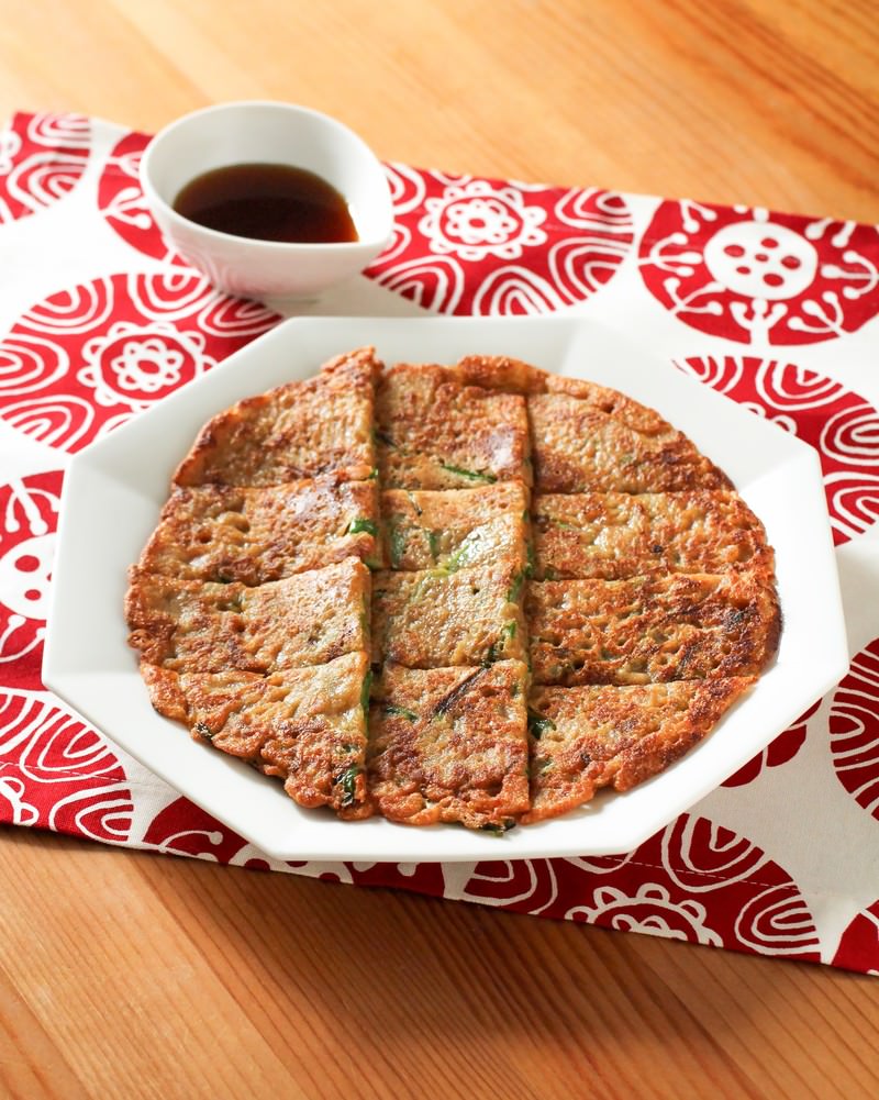 白い八角形の皿に焼き色のついたチヂミが切り分けられ奥にタレの小皿がある