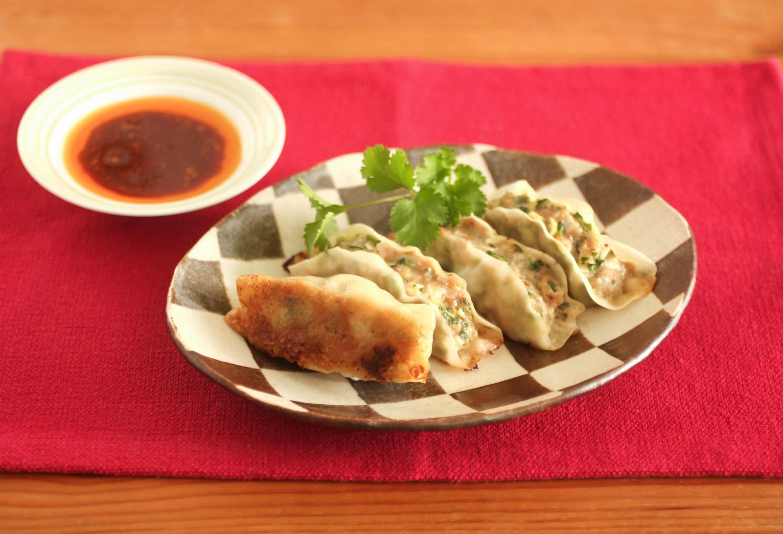 茶色と白のしま模様の皿に焼き餃子が5つ盛られ奥に味噌だれの小皿がある