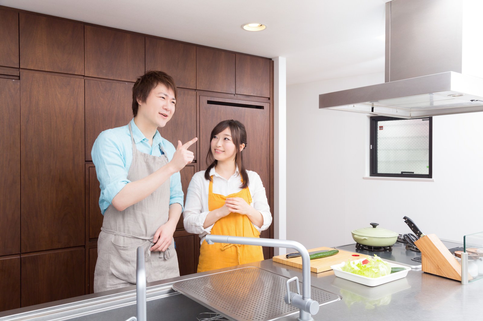 キッチンで一緒に料理をする男性と女性。男性が説明し、女性がサラダの準備をしている。［モデル：五十嵐夫妻］